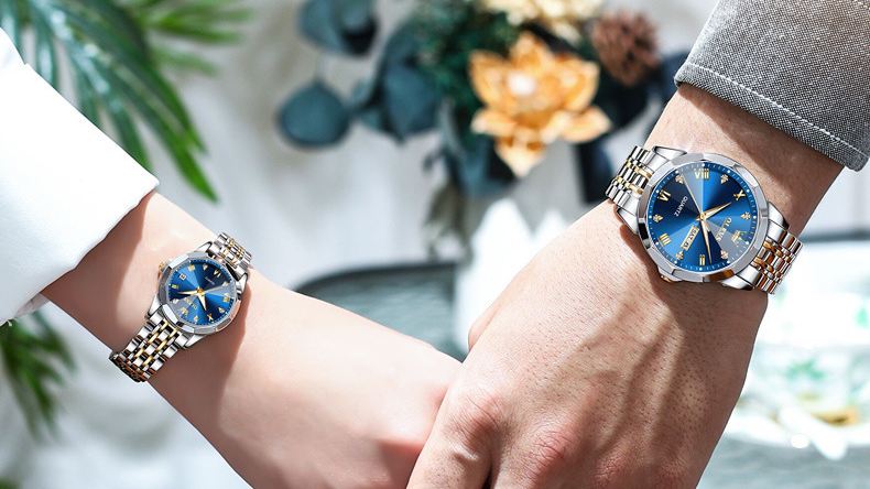 A couple holding hands wearing matching OLEVS blue dial watches.